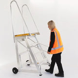 Person in an orange safety vest using a stockmaster step-thru ladder on a white background