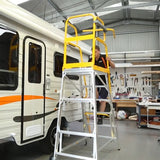 Person using a Stockmaster TrackerPRO All-Terrain Mobile Platform Ladder to work on a recreational vehicle in a workshop.